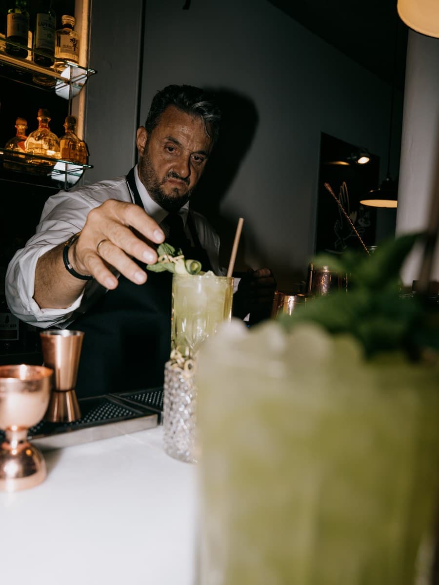 Búho service: a bartender garnishing a signature cocktail at the bar, premium spirits visible behind.